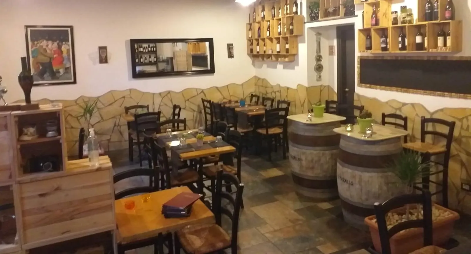 La sala: muretto in pietra, sedie impagliate, botti usate come tavoli e cassette di vino alle pareti